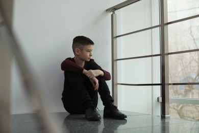 Photo of Upset preteen boy sitting on staircase indoors