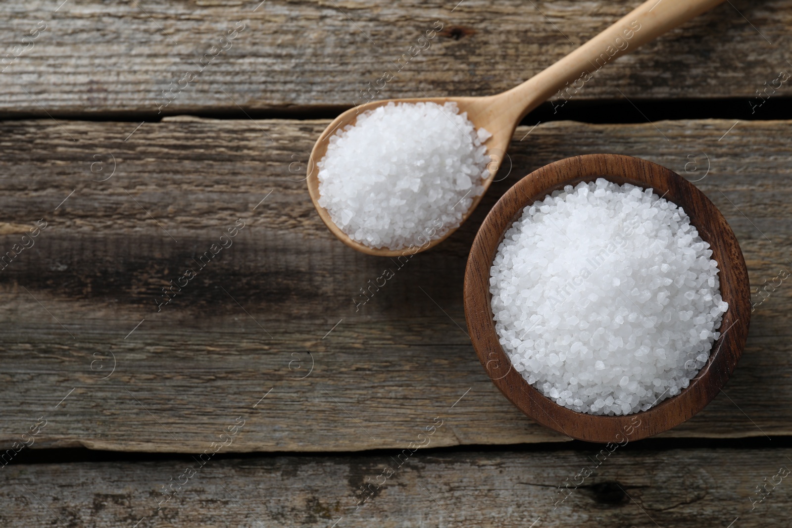 Photo of Organic salt in bowl and spoon on wooden table, flat lay. Space for text