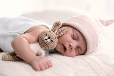 Photo of Adorable newborn baby with toy bunny sleeping on white knitted plaid