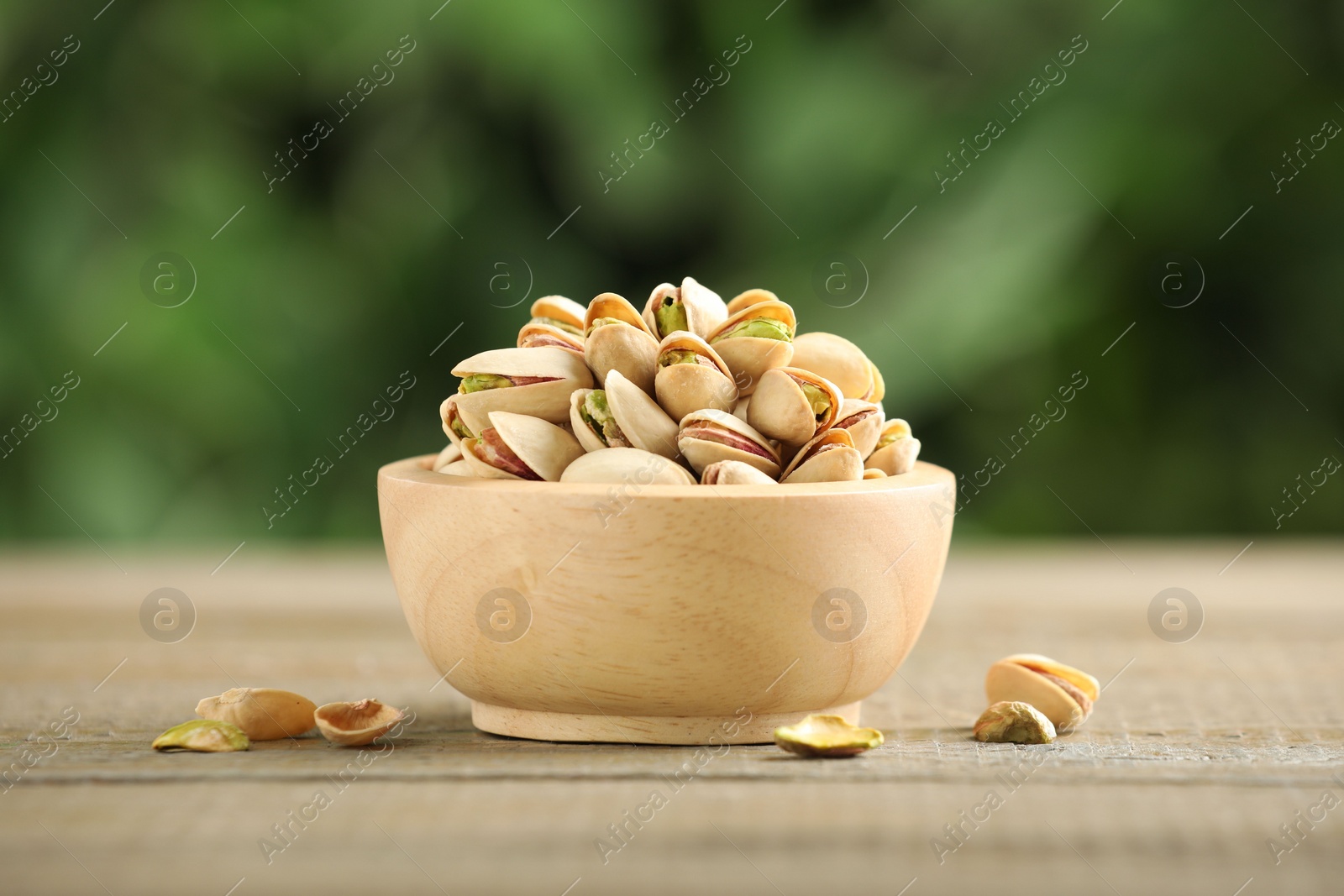 Photo of Tasty pistachios in bowl on wooden table against blurred background, closeup