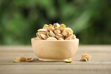 Tasty pistachios in bowl on wooden table against blurred background, closeup