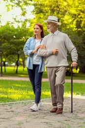 Photo of Senior man with walking cane and young woman in park
