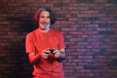 Photo of Emotional mature man playing video games with controller near brick wall. Space for text