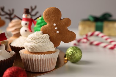Photo of Tasty Christmas cupcake with gingerbread man and baubles on white table. Space for text