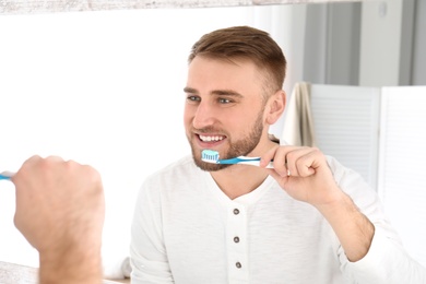 Photo of Young man cleaning teeth against mirror in bathroom