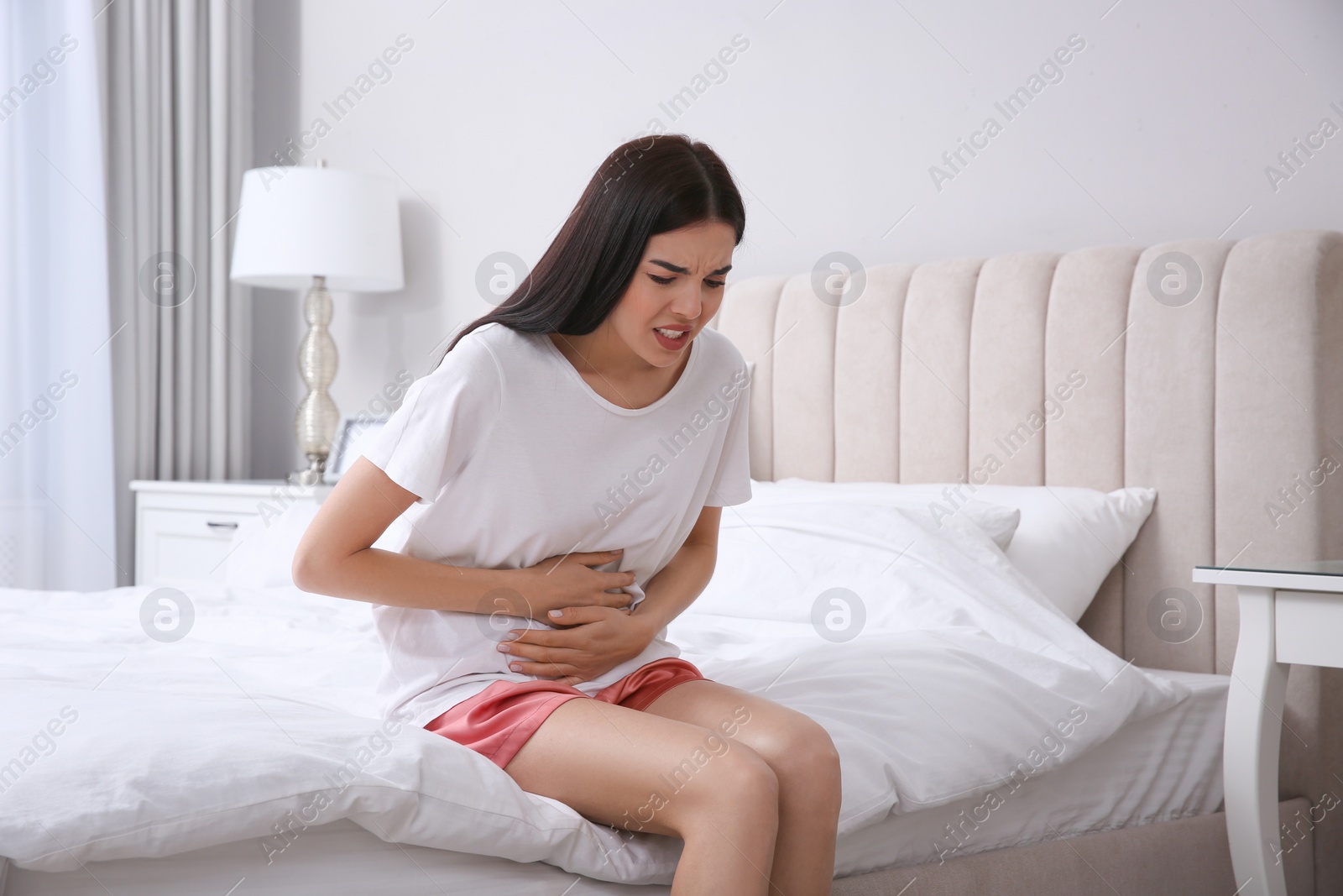 Photo of Young woman suffering from stomach ache in bedroom