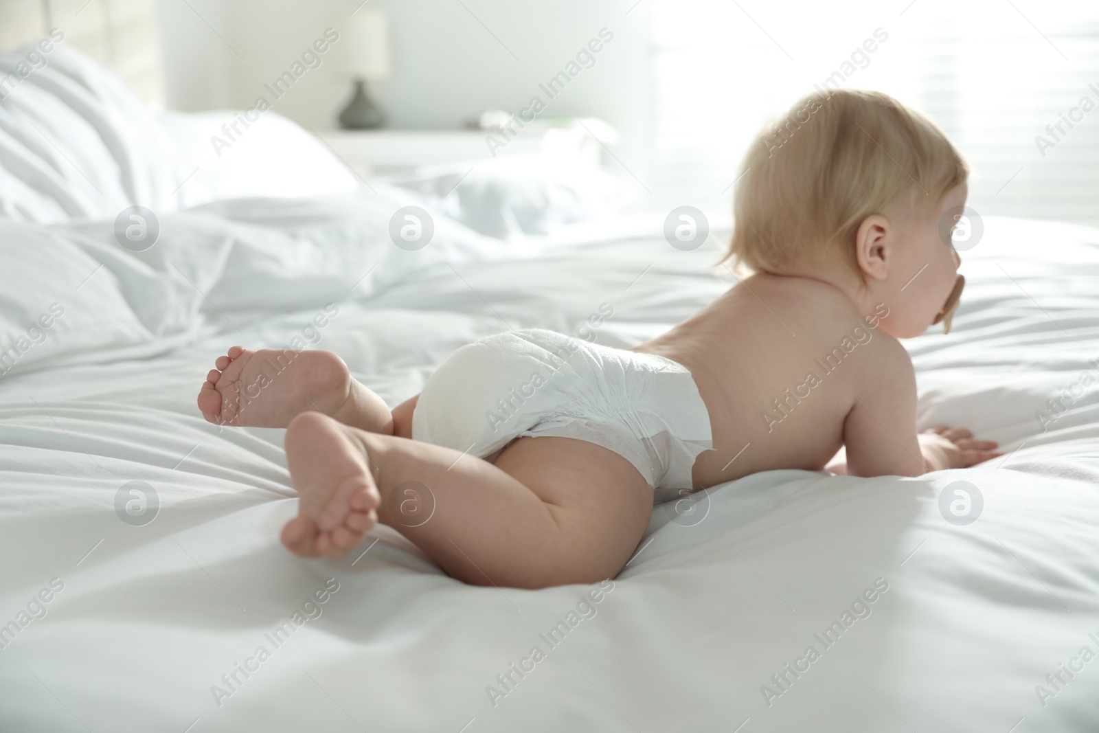 Photo of Cute little baby in diaper lying on bed at home