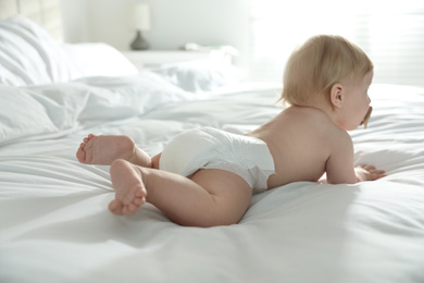 Photo of Cute little baby in diaper lying on bed at home