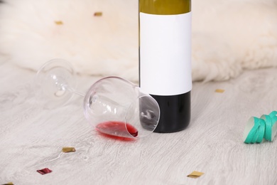 Photo of Overturned glass and bottle of wine on messy floor indoors. After party chaos