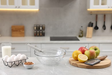 Metal whisk, bowl, grater and different products on gray marble table in kitchen