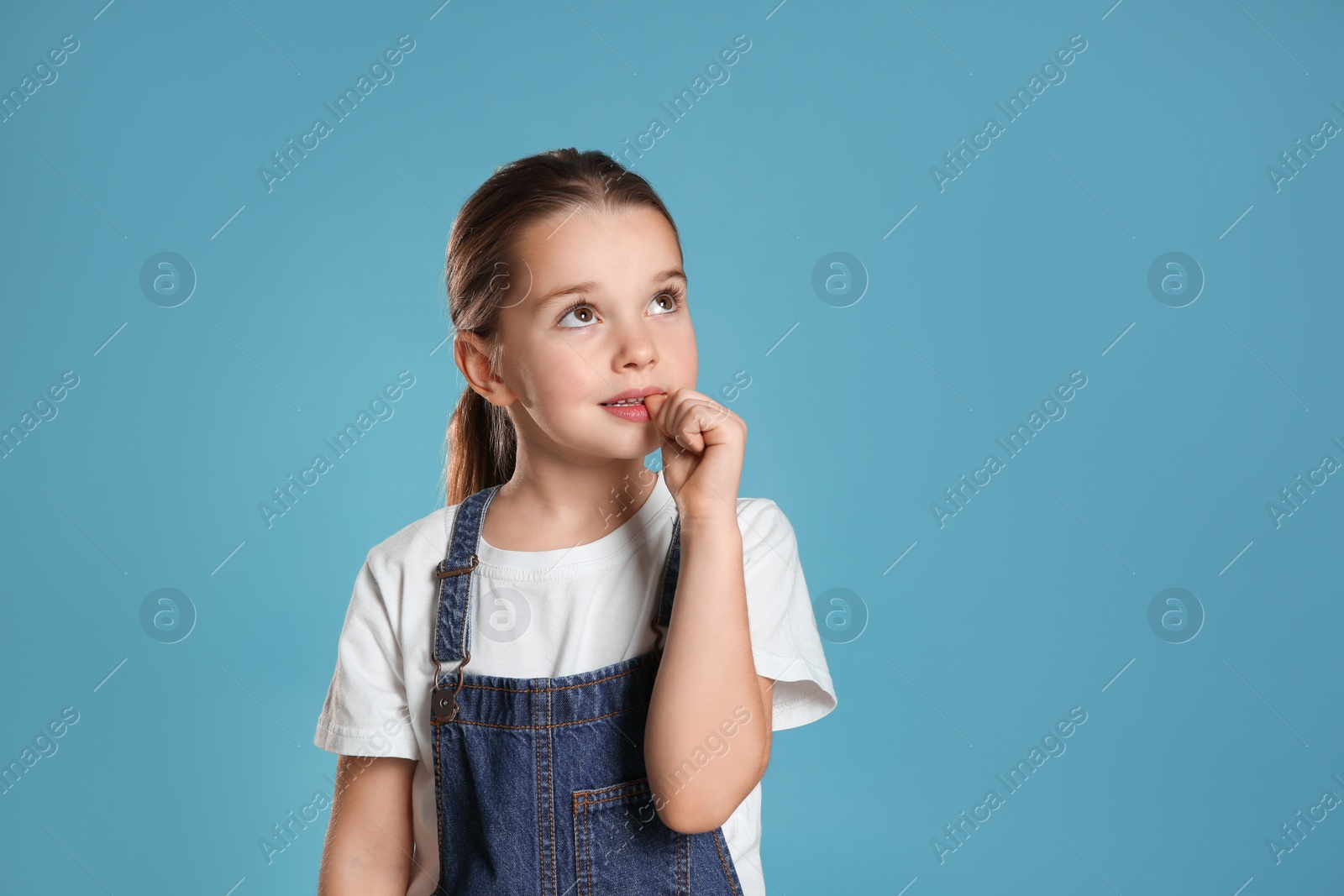 Photo of Cute little girl biting her nails on turquoise background, space for text