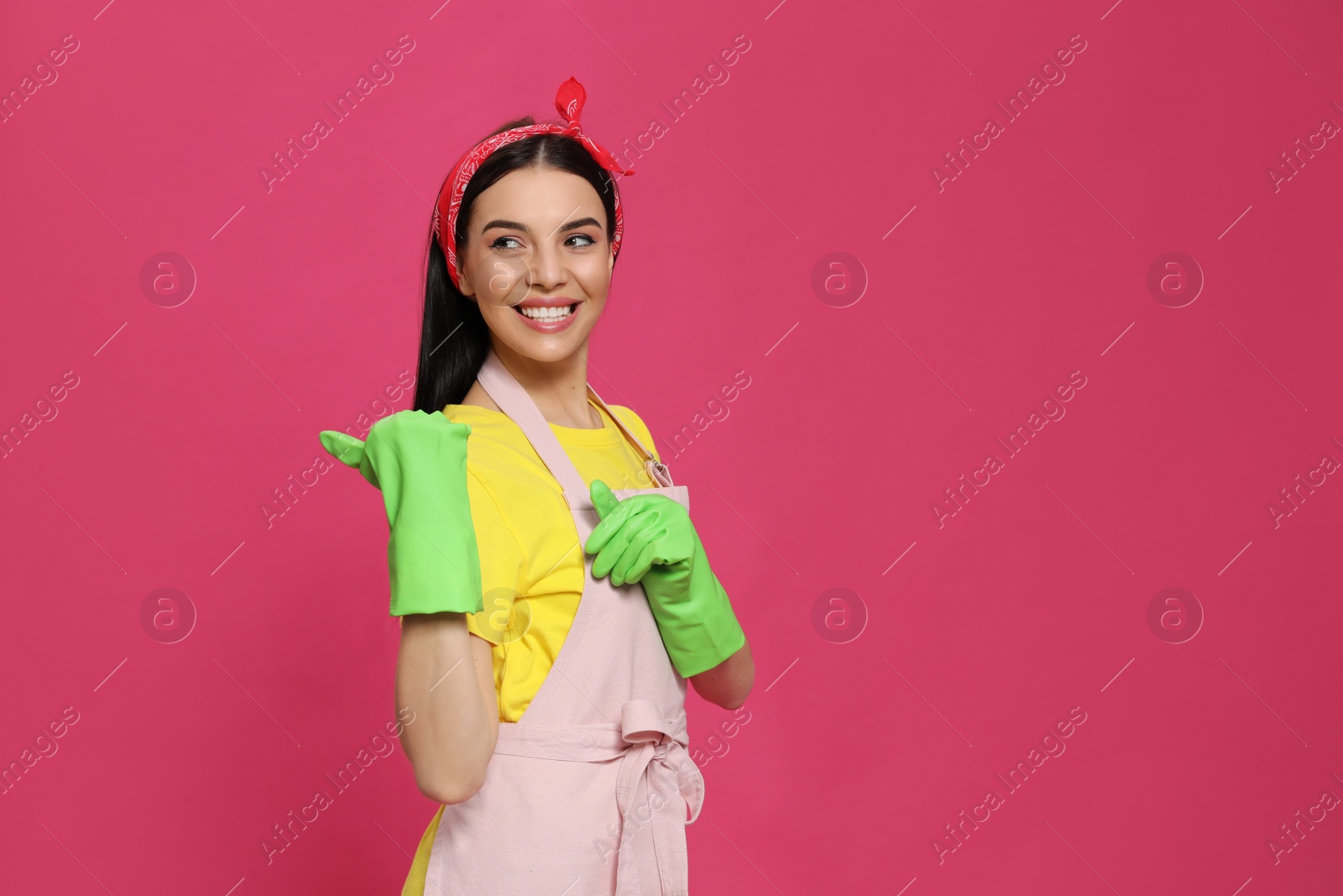 Photo of Young housewife wearing rubber gloves on pink background, space for text