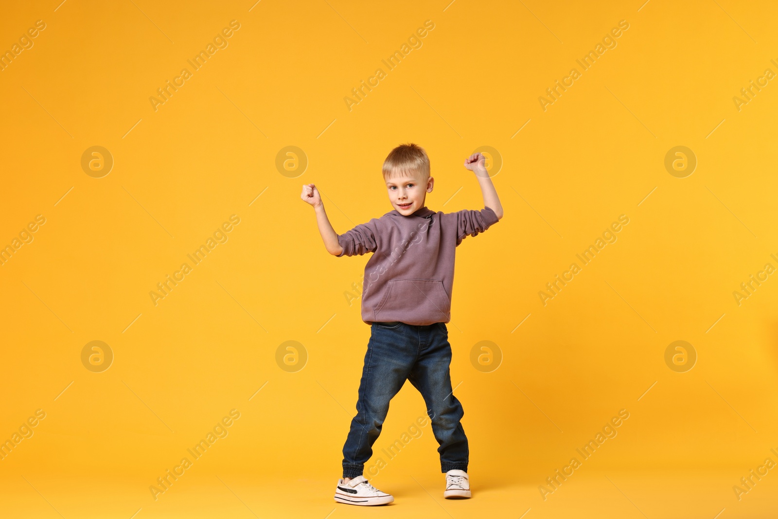 Photo of Happy little boy dancing on yellow background. Space for text