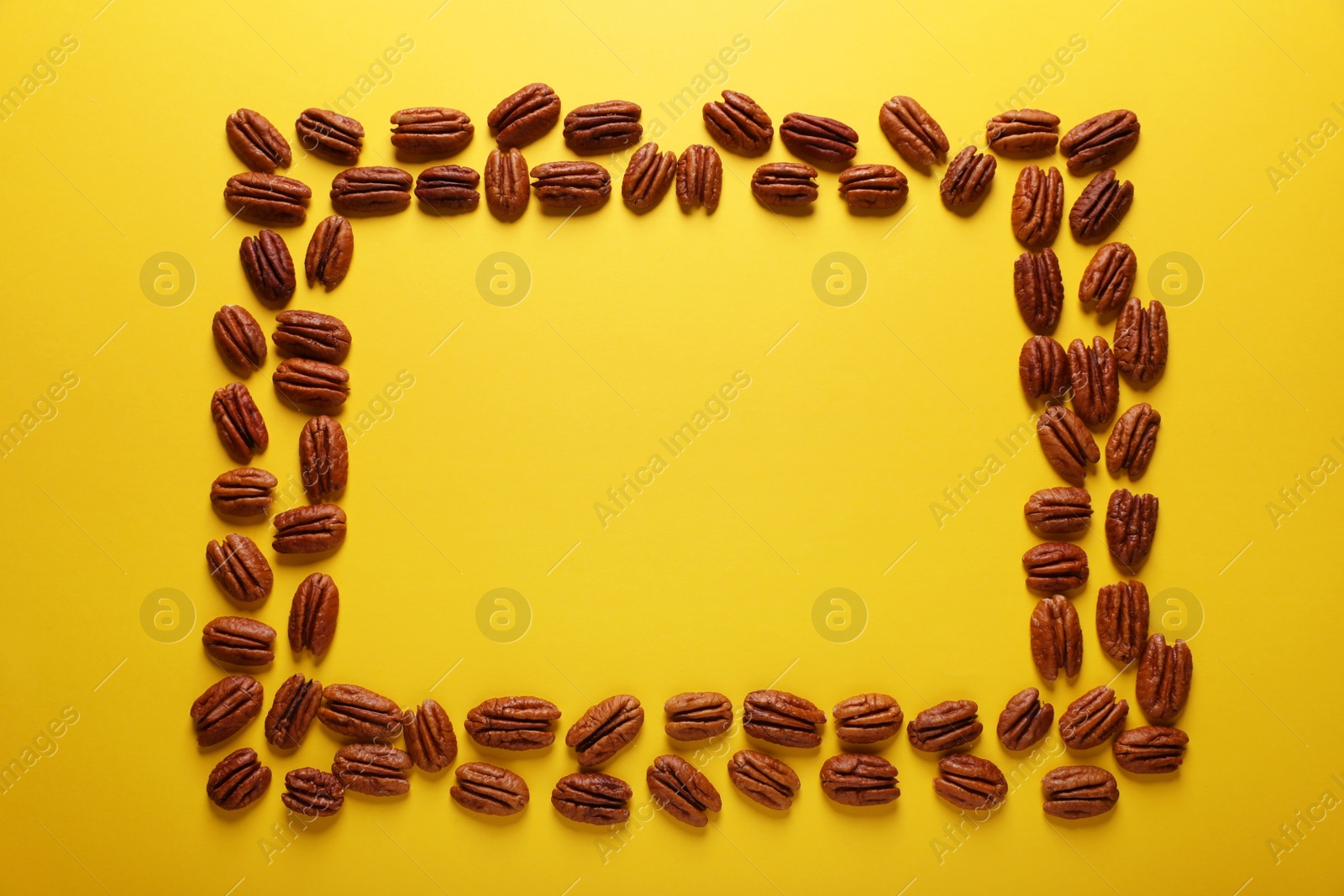 Photo of Frame of tasty pecan nuts on yellow background, flat lay. Space for text