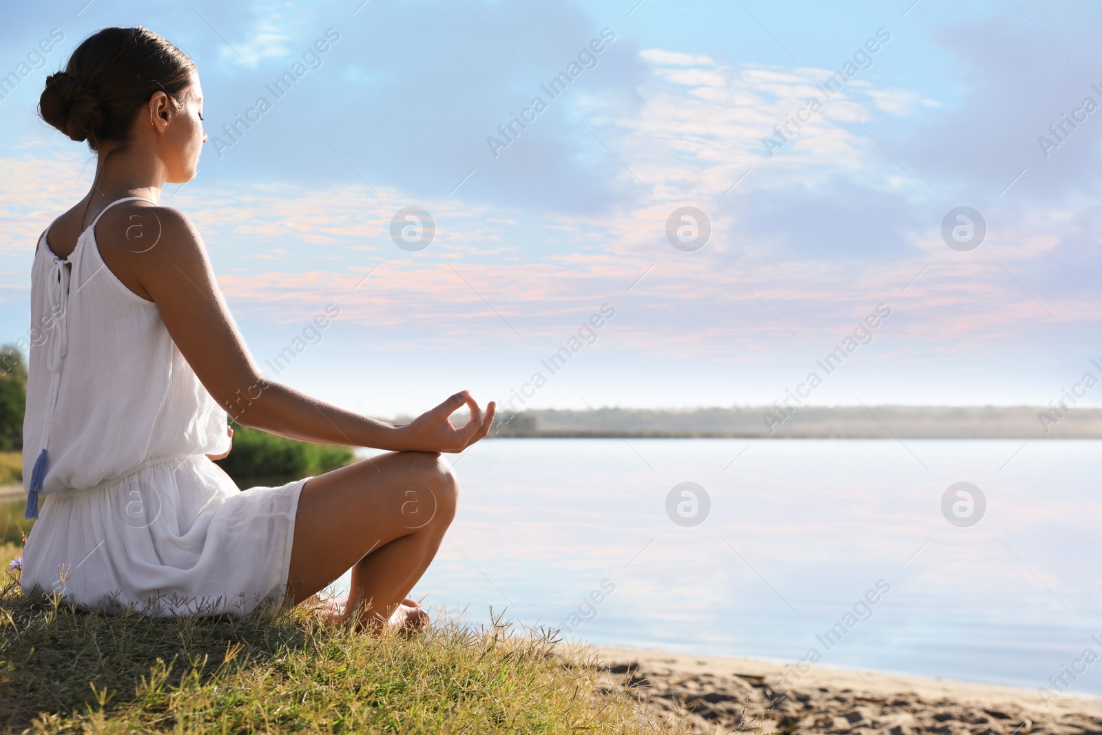 Photo of Young woman meditating near river at sunset, space for text. Nature healing power