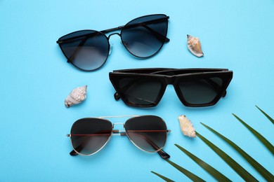 Photo of Stylish sunglasses and seashells on light blue background, flat lay