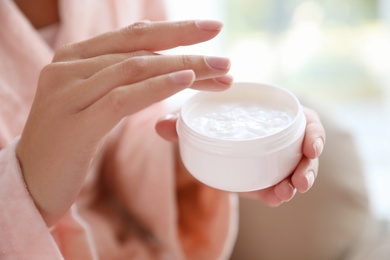 Photo of Woman with jar of moisturizing cream on blurred background, closeup