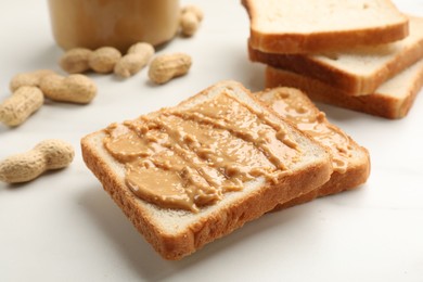 Photo of Delicious toasts with peanut butter and nuts on white table, closeup