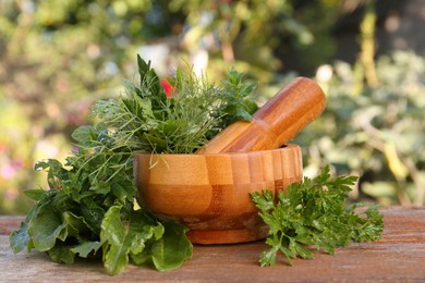 Mortar, pestle and different herbs on wooden table outdoors, closeup
