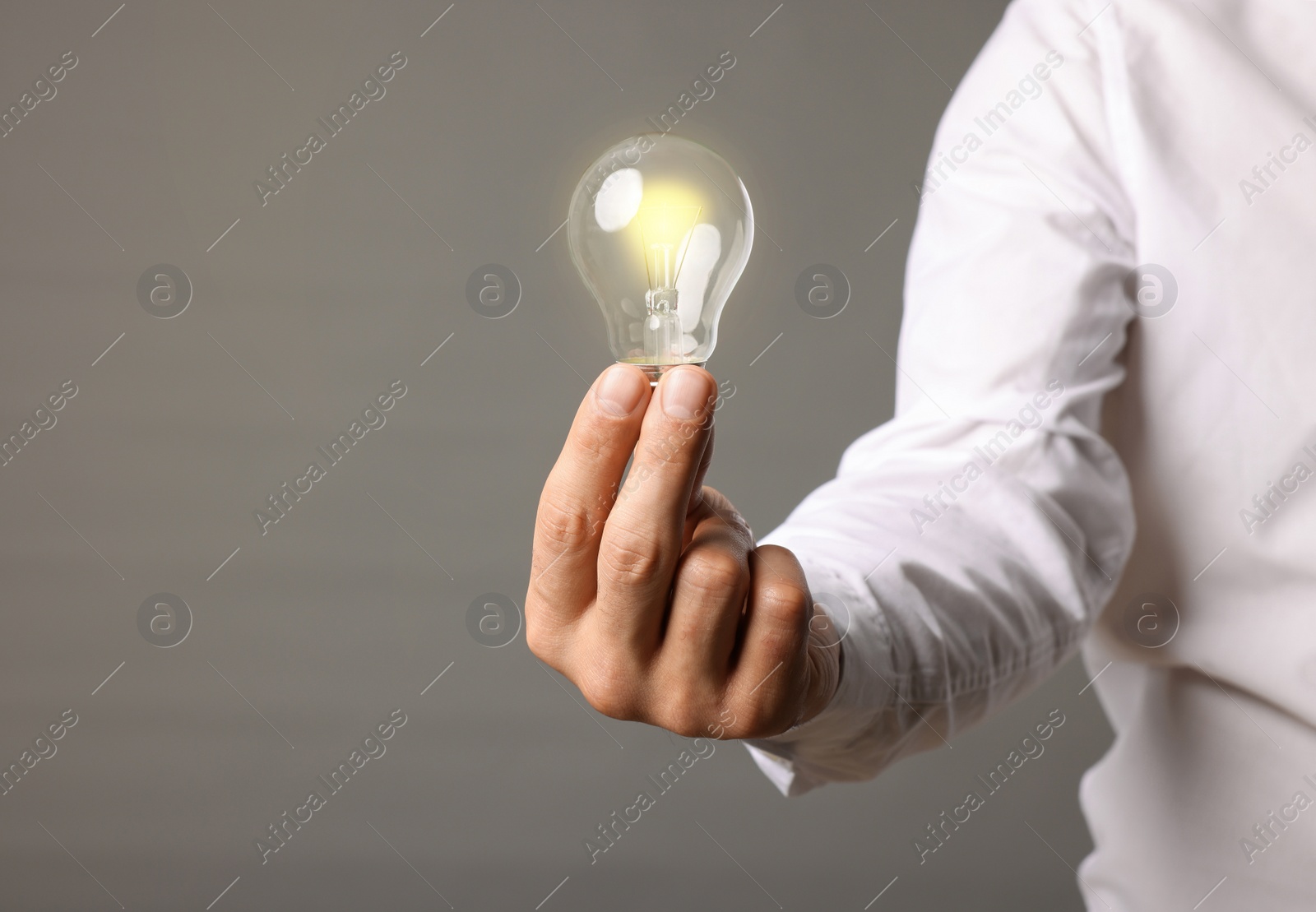 Photo of Glow up your ideas. Closeup view of man holding light bulb on grey background, space for text