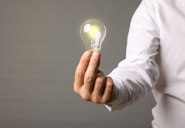 Photo of Glow up your ideas. Closeup view of man holding light bulb on grey background, space for text