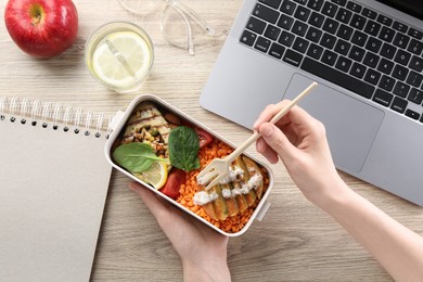 Woman eating healthy products high in vegetable fats near laptop at wooden table, top view