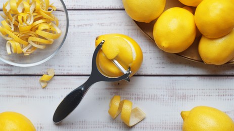 Bowl with peel pieces, fresh lemons and zester on white wooden table, flat lay