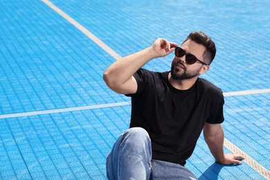 Photo of Handsome man in sunglasses on blue floor covering outdoors, space for text