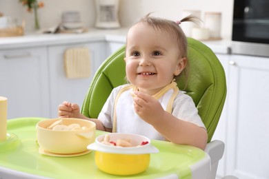 Photo of Cute little baby eating food in high chair at kitchen