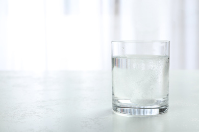 Woman putting tablet into glass of water indoors, space for text