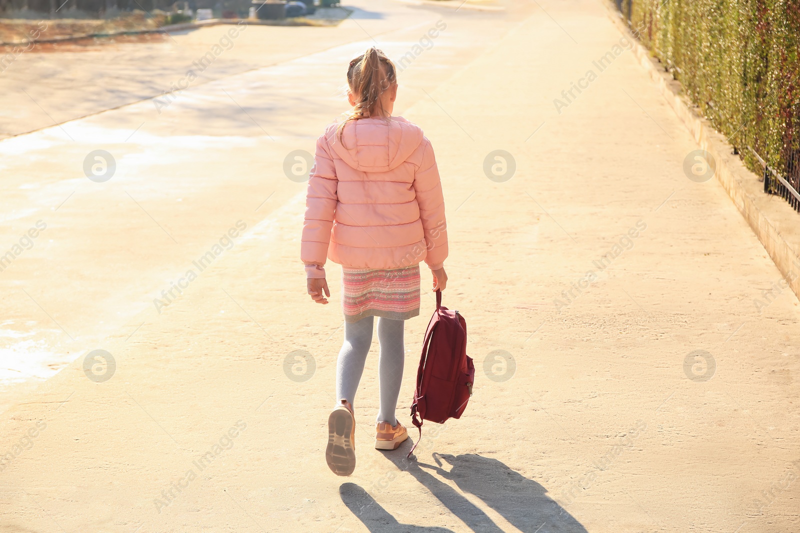 Photo of Cute little girl with backpack on city street, back view