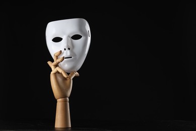 Photo of Wooden mannequin hand holding plastic mask on black background, space for text. Theatrical performance
