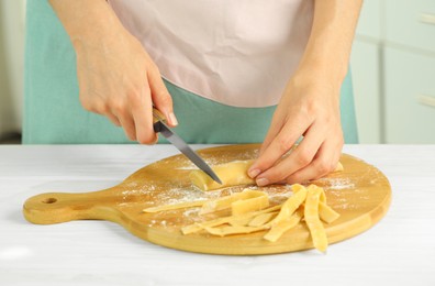 Photo of Making homemade pasta. Woman cutting dough at white wooden table, closeup