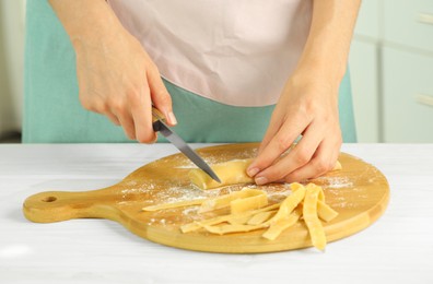 Making homemade pasta. Woman cutting dough at white wooden table, closeup