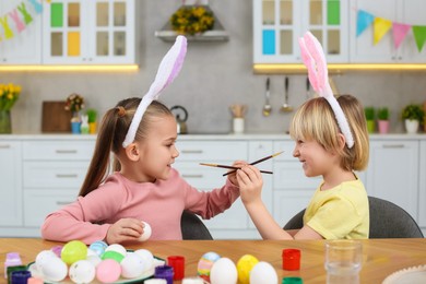 Photo of Children having fun while painting Easter eggs at table in kitchen