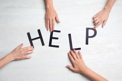 People making word "HELP" of letters on light background, top view