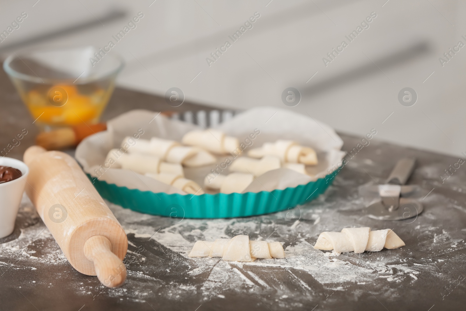 Photo of Baking dish with raw croissants on table in kitchen