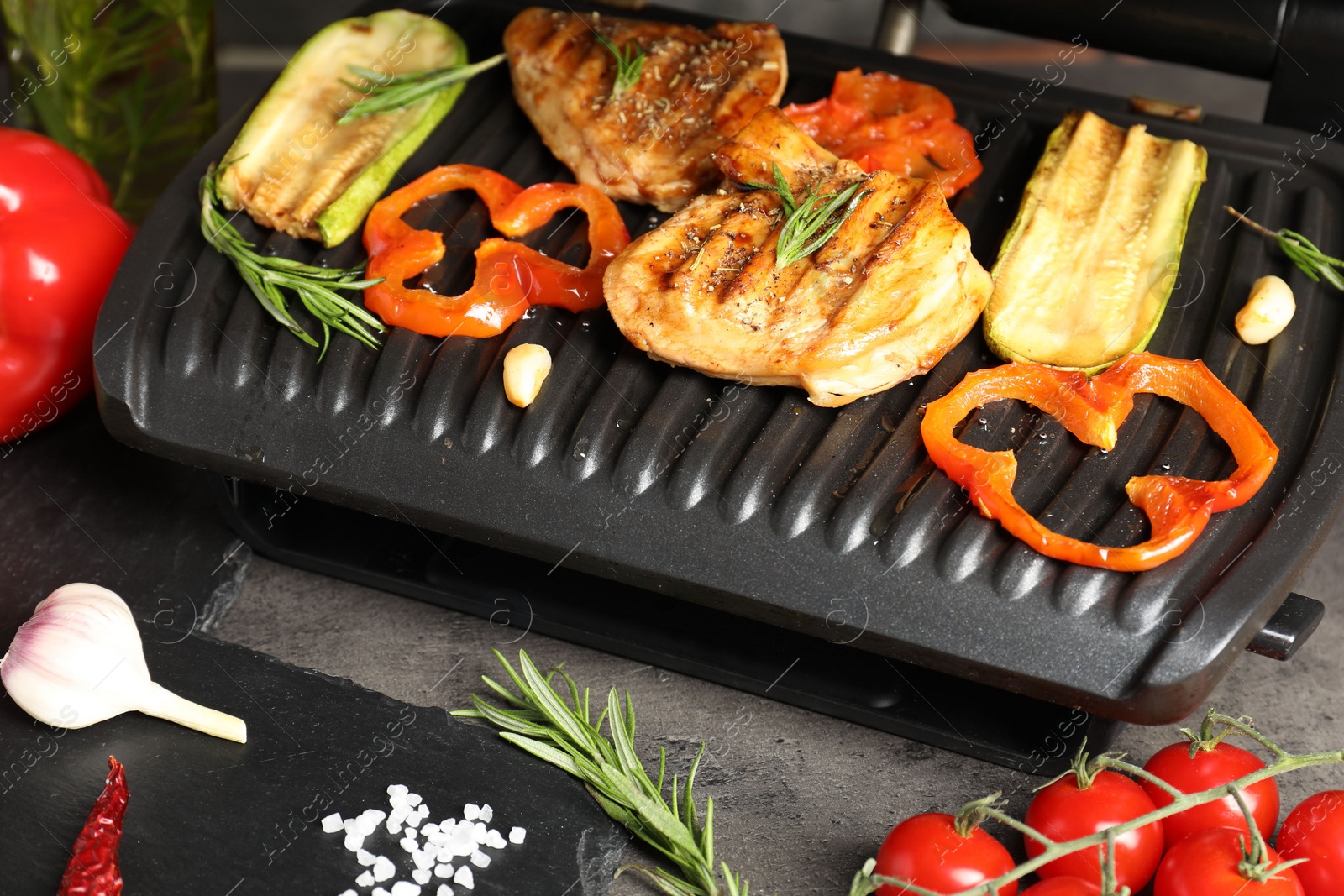 Photo of Electric grill with tasty meat, spices and vegetables on grey table