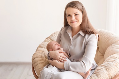 Photo of Young mother with her newborn baby in papasan chair at home