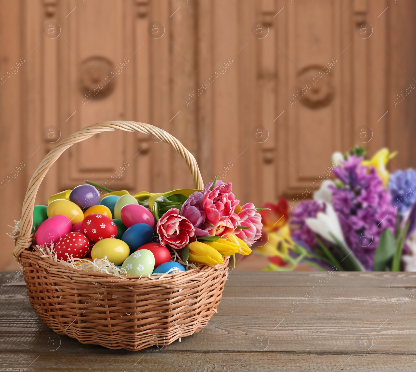 Image of Wicker basket with bright painted Easter eggs on wooden table indoors, space for text 