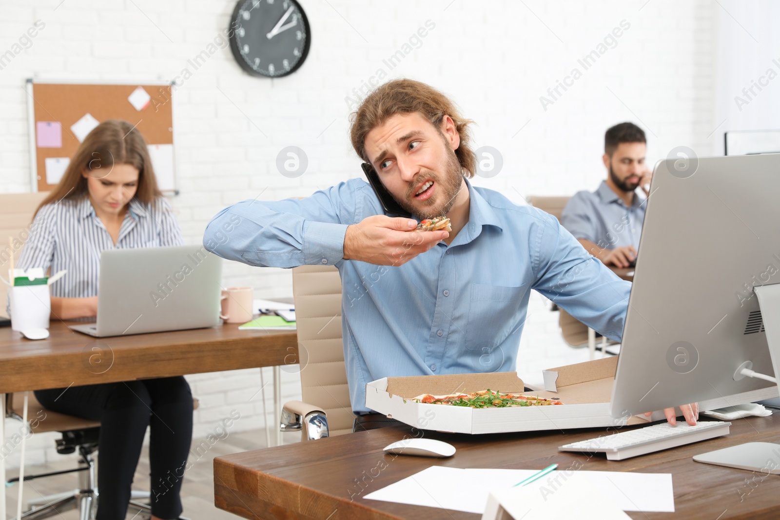 Photo of Office employee having pizza for lunch while talking on phone at workplace. Food delivery
