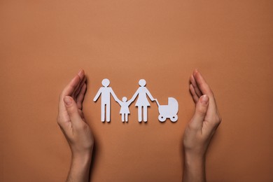 Photo of Woman protecting paper family figures on brown background, top view. Insurance concept