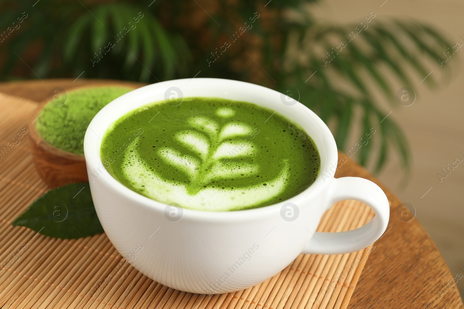 Photo of Delicious matcha latte in cup and powder on wooden coffee table, closeup