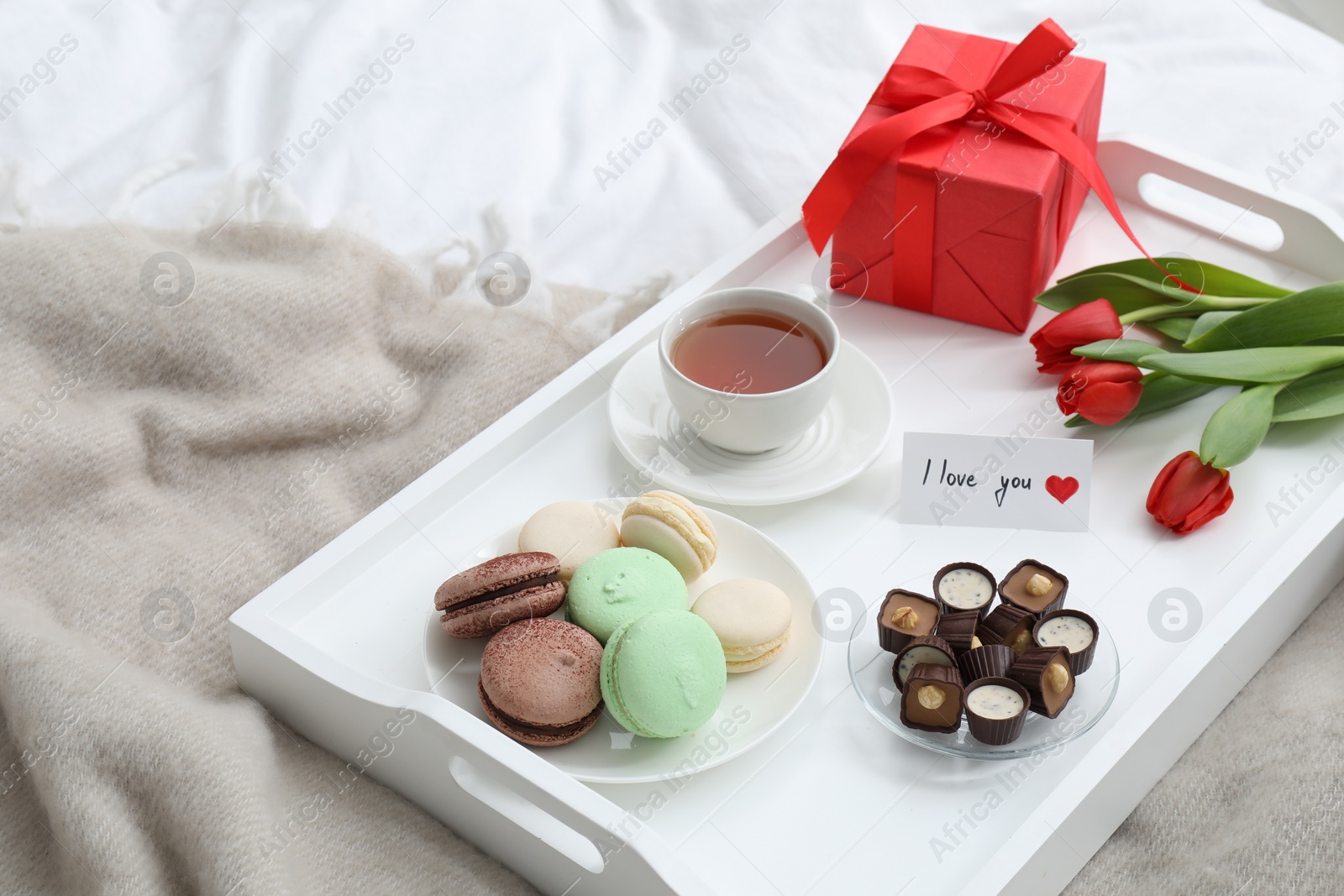 Photo of Tasty breakfast served in bed. Delicious desserts, tea, gift box, flowers and I Love You card on tray