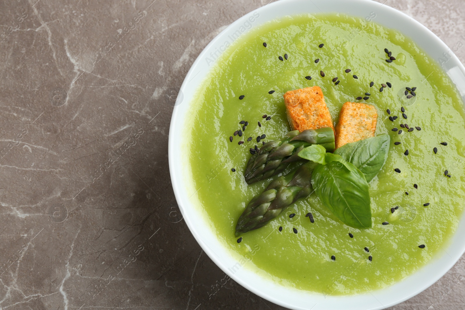 Photo of Delicious asparagus soup in bowl on grey marble table, top view