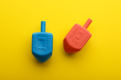 Photo of Colorful dreidels on yellow background, flat lay. Traditional Hanukkah game