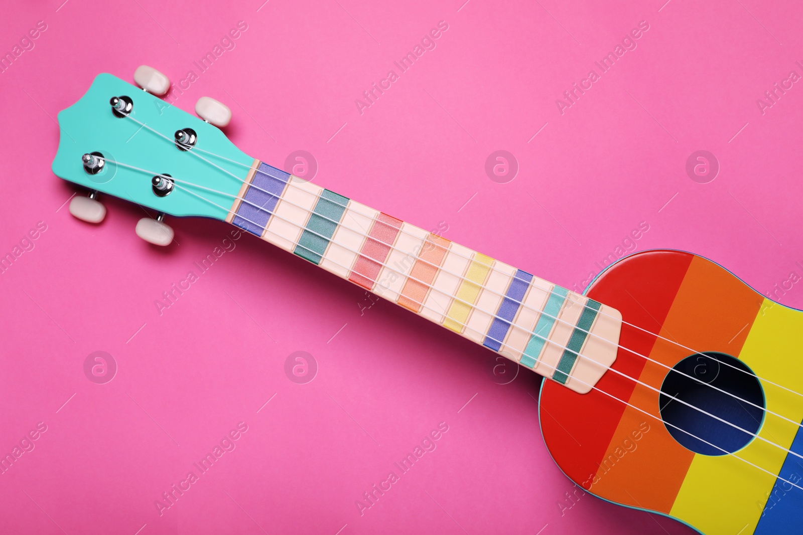 Photo of Colorful ukulele on pink background, top view. String musical instrument