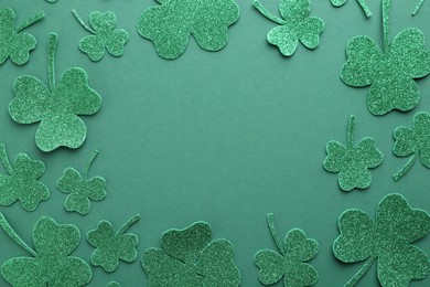 St. Patrick's day. Frame of shiny decorative clover leaves on green background, flat lay. Space for text