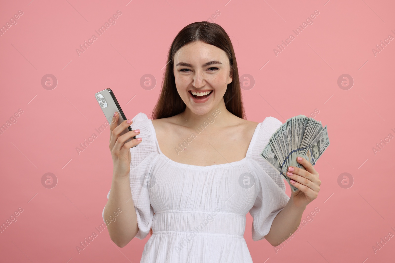 Photo of Happy woman with dollar banknotes and smartphone on pink background