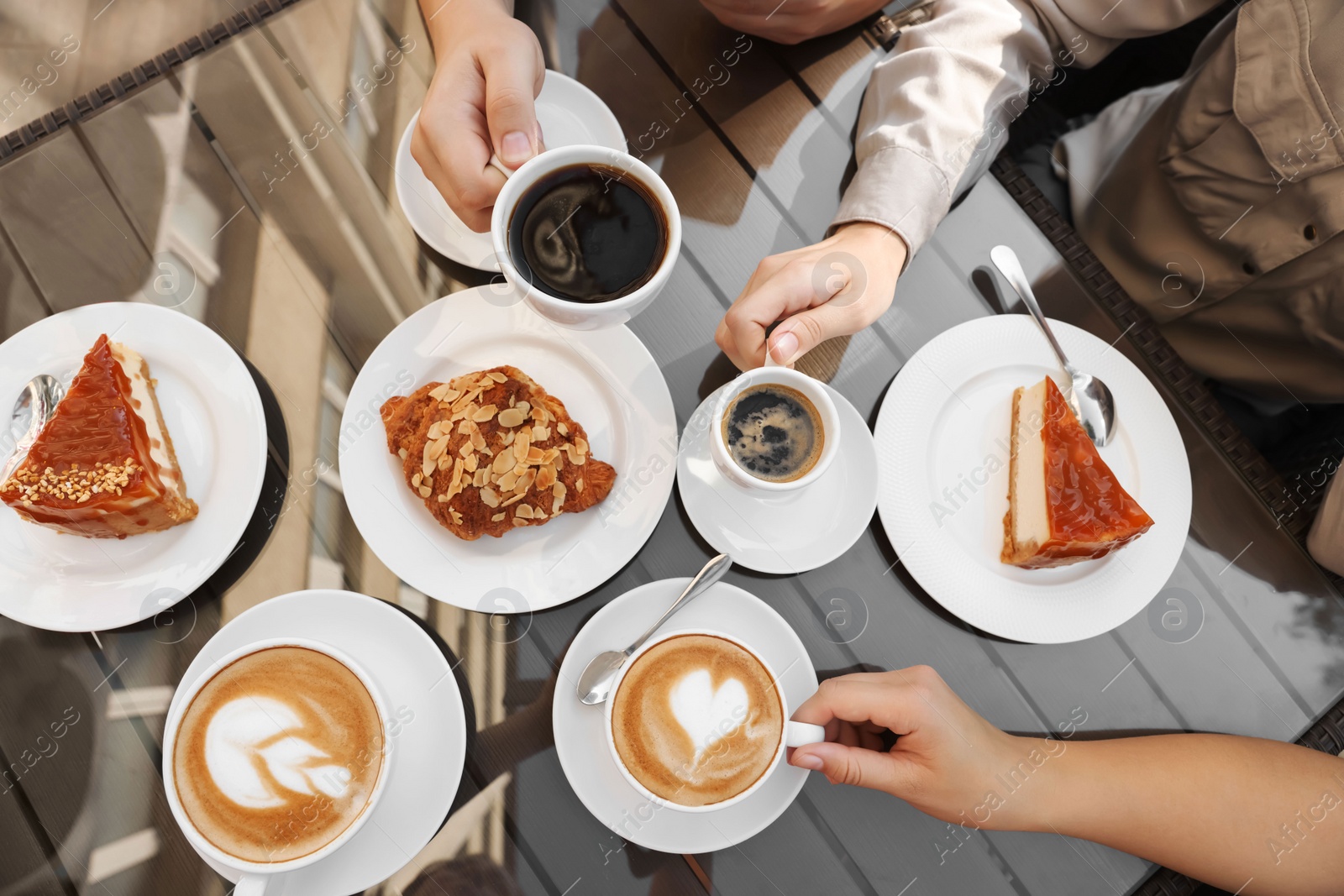 Photo of Friends drinking coffee at wooden table in outdoor cafe, top view